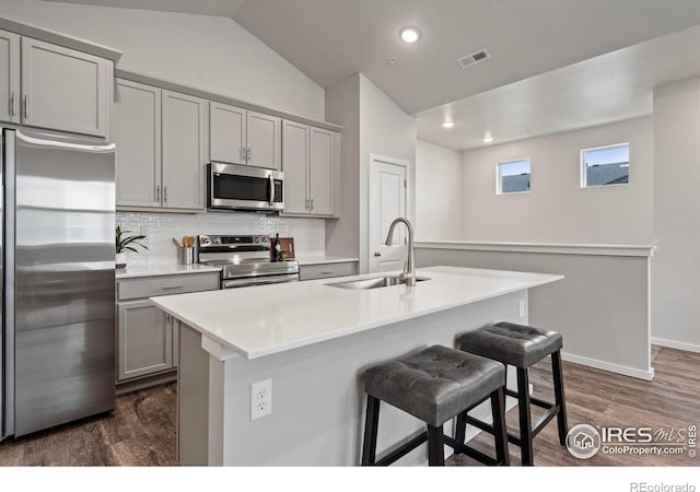 kitchen with a center island with sink, sink, appliances with stainless steel finishes, gray cabinetry, and vaulted ceiling