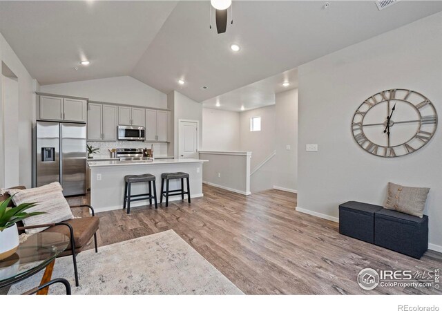 kitchen with light hardwood / wood-style floors, a center island with sink, lofted ceiling, and appliances with stainless steel finishes