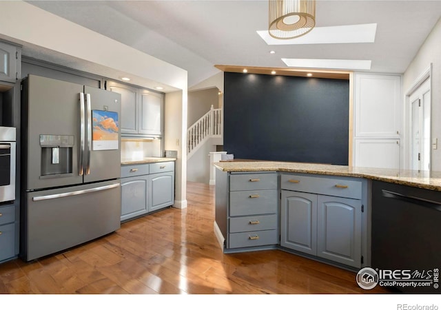 kitchen with hardwood / wood-style flooring, light stone countertops, a skylight, gray cabinetry, and stainless steel appliances