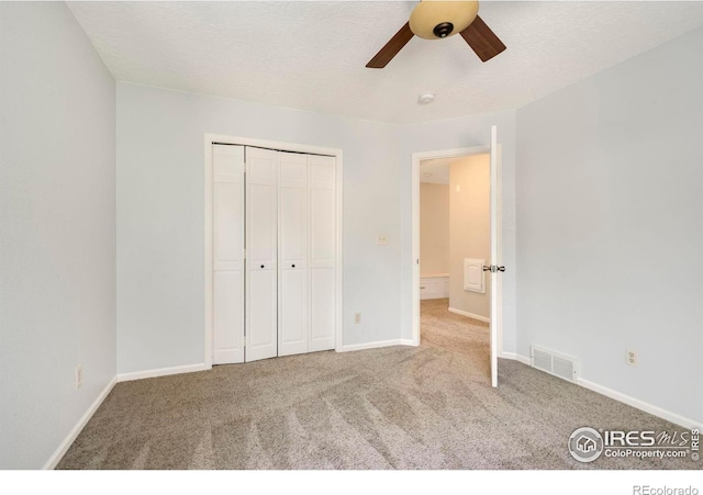 unfurnished bedroom with a textured ceiling, carpet flooring, a closet, and ceiling fan