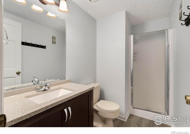 bathroom featuring vanity, toilet, a textured ceiling, and a shower with door