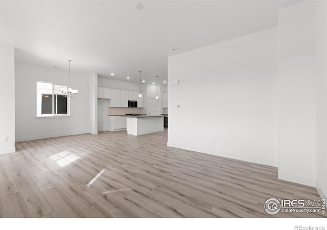 unfurnished living room with an inviting chandelier and light hardwood / wood-style flooring