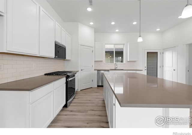 kitchen with appliances with stainless steel finishes, white cabinets, hanging light fixtures, and light hardwood / wood-style floors