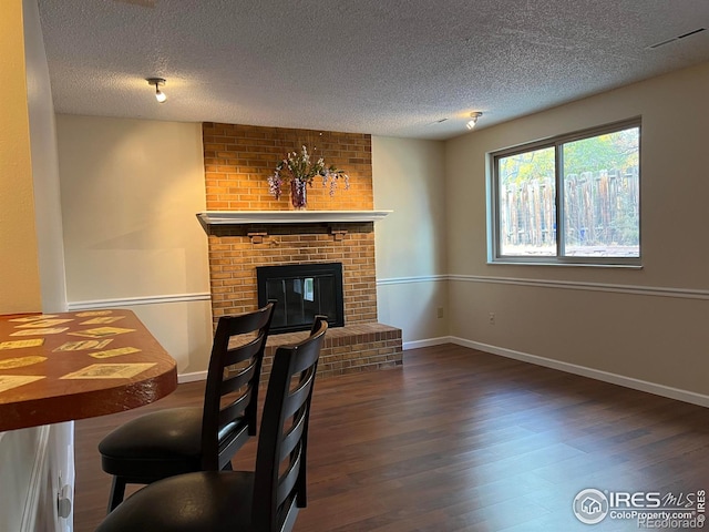 living room with dark hardwood / wood-style flooring, a textured ceiling, and a brick fireplace