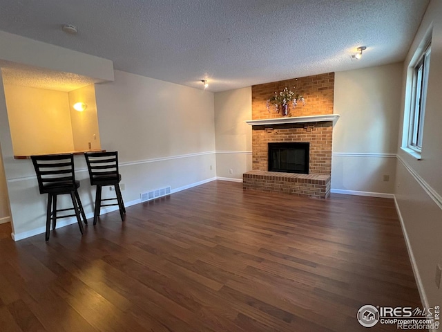 unfurnished living room featuring dark wood-type flooring, a textured ceiling, and a brick fireplace