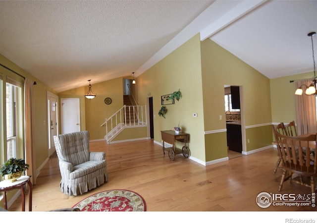 living room with light hardwood / wood-style floors, a textured ceiling, lofted ceiling with beams, and a notable chandelier