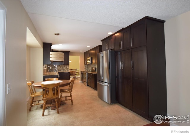 kitchen featuring appliances with stainless steel finishes, dark brown cabinets, hanging light fixtures, sink, and decorative backsplash