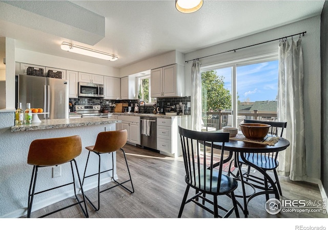 kitchen with decorative backsplash, white cabinets, appliances with stainless steel finishes, light hardwood / wood-style floors, and sink