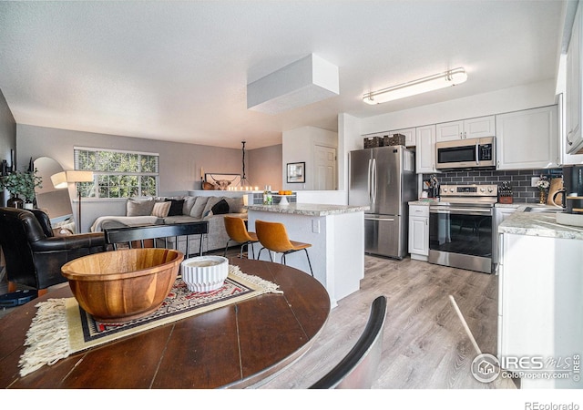 kitchen featuring white cabinets, decorative backsplash, appliances with stainless steel finishes, a kitchen breakfast bar, and light hardwood / wood-style flooring