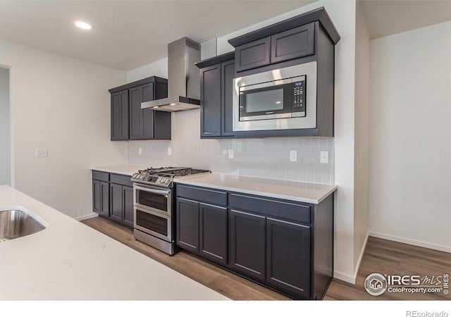 kitchen with appliances with stainless steel finishes, dark hardwood / wood-style floors, sink, backsplash, and wall chimney exhaust hood