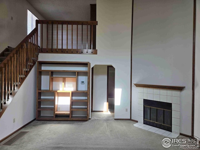 unfurnished living room featuring a towering ceiling, a tiled fireplace, and carpet