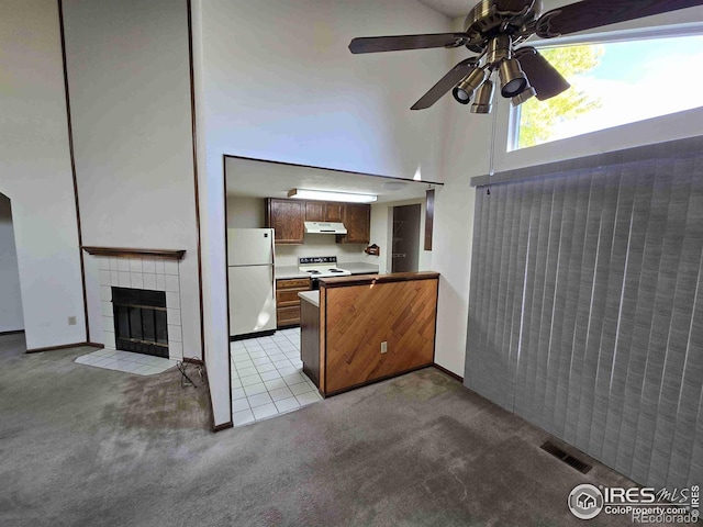 unfurnished living room with a towering ceiling, a tiled fireplace, light colored carpet, and ceiling fan