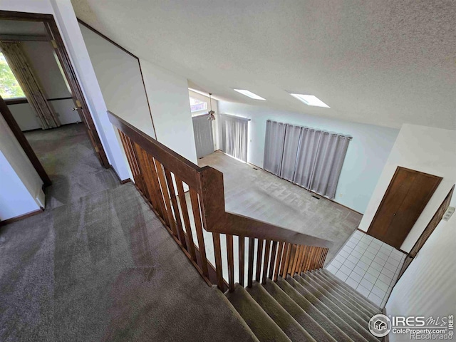 stairway with a skylight, ceiling fan, a textured ceiling, and carpet flooring