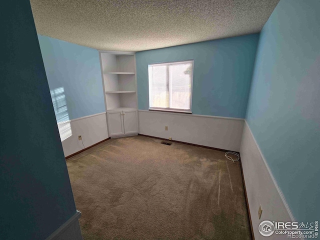 carpeted spare room featuring a textured ceiling and built in shelves