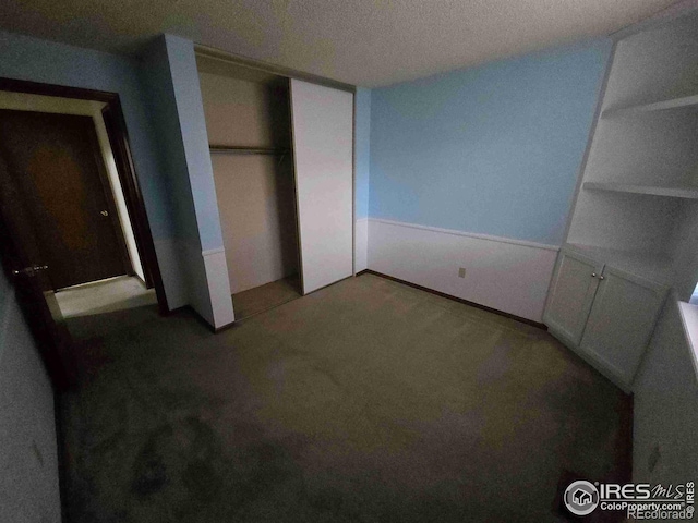 unfurnished bedroom featuring a closet, a textured ceiling, and dark colored carpet