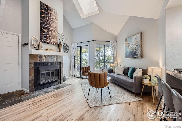 living room featuring vaulted ceiling with skylight, hardwood / wood-style floors, and a tile fireplace