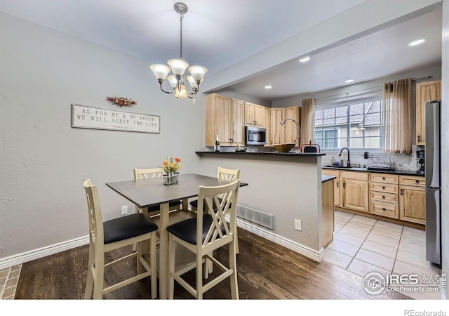 interior space with light wood-type flooring, hanging light fixtures, stainless steel appliances, a breakfast bar area, and a chandelier