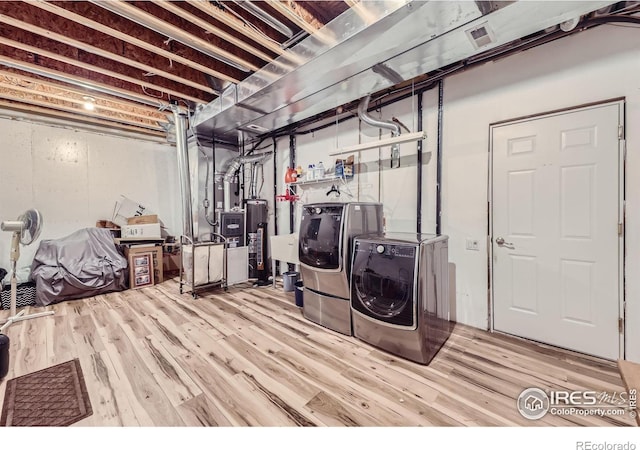 clothes washing area featuring washing machine and dryer, water heater, wood finished floors, and laundry area