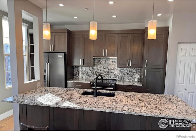 kitchen featuring high end refrigerator, decorative backsplash, sink, decorative light fixtures, and light stone counters