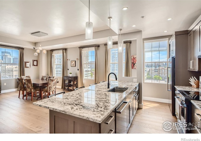 kitchen featuring light wood-type flooring, an island with sink, stainless steel appliances, pendant lighting, and light stone counters