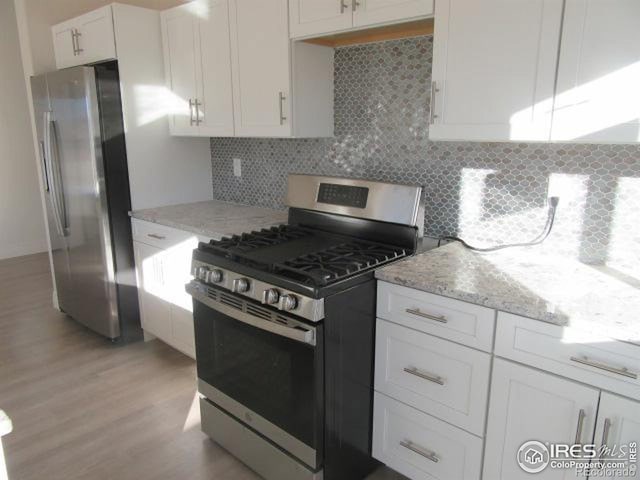 kitchen featuring backsplash, light hardwood / wood-style floors, white cabinetry, light stone countertops, and stainless steel appliances