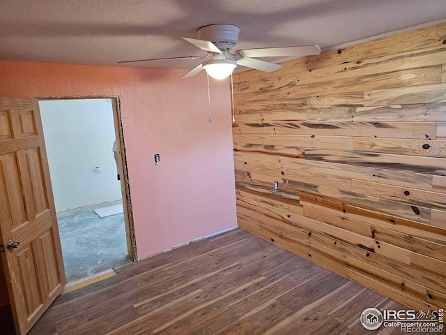 spare room with a textured ceiling, hardwood / wood-style floors, wooden walls, and ceiling fan