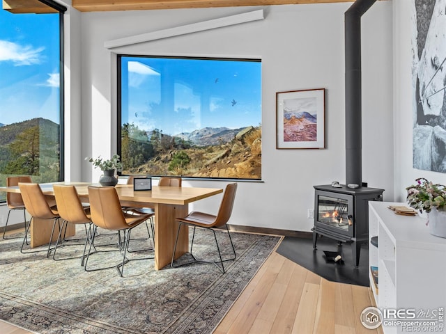 dining space featuring a wood stove, wood-type flooring, plenty of natural light, and vaulted ceiling