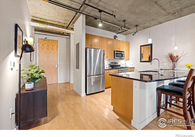 kitchen featuring stainless steel appliances, dark stone counters, hanging light fixtures, sink, and light hardwood / wood-style floors