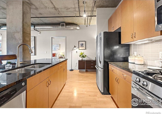 kitchen featuring light hardwood / wood-style floors, stainless steel appliances, dark stone counters, sink, and backsplash