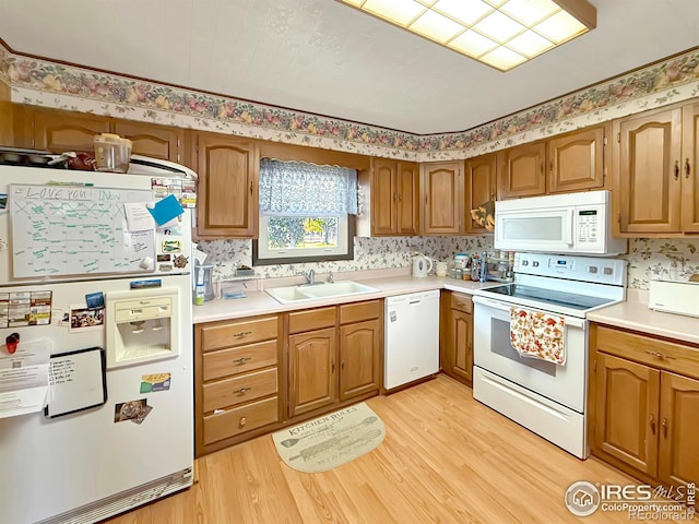 kitchen with brown cabinets, light countertops, a sink, light wood-type flooring, and white appliances