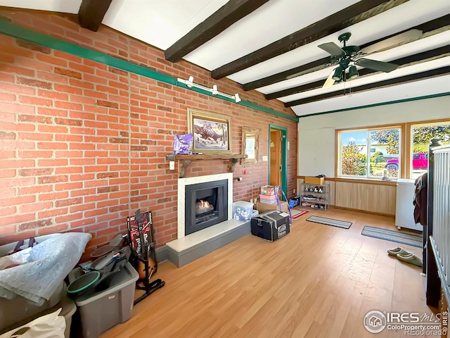 living room featuring a fireplace, light wood finished floors, lofted ceiling with beams, a ceiling fan, and brick wall