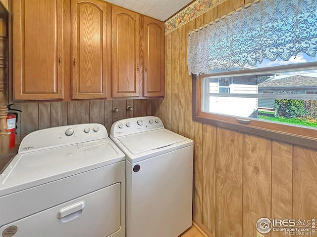 laundry room featuring washing machine and dryer, cabinet space, and wood walls