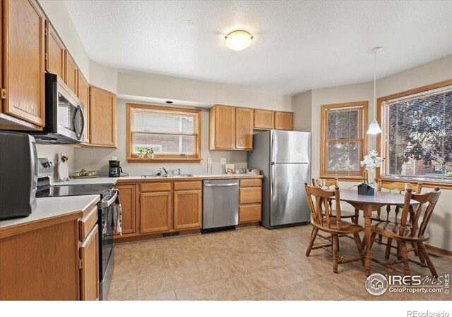 kitchen with decorative light fixtures, stainless steel appliances, a textured ceiling, light countertops, and a sink