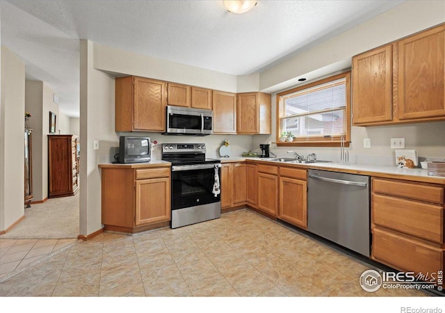 kitchen featuring a textured ceiling, stainless steel appliances, a sink, and light countertops