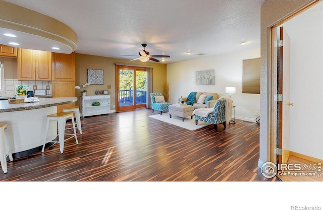 living room with dark wood-type flooring, ceiling fan, and a textured ceiling