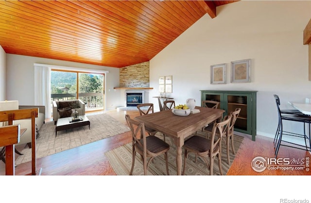 dining area featuring a stone fireplace, wood-type flooring, wooden ceiling, high vaulted ceiling, and beam ceiling