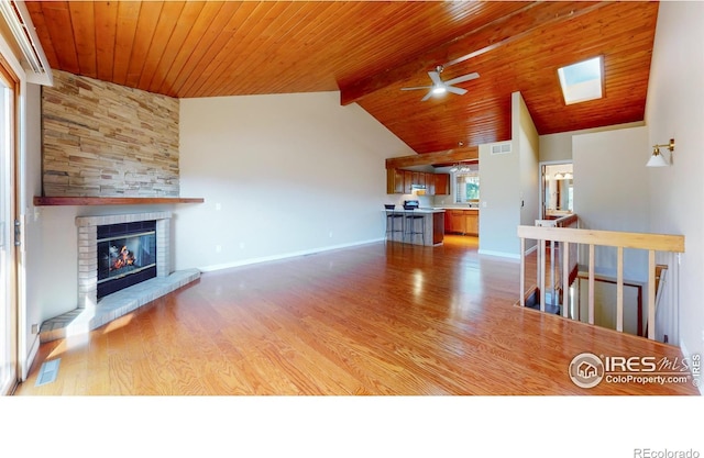 unfurnished living room featuring lofted ceiling with skylight, wood ceiling, a large fireplace, and light hardwood / wood-style floors