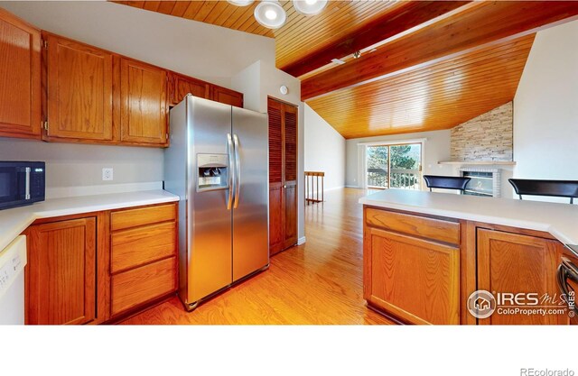 kitchen with stainless steel refrigerator with ice dispenser, a stone fireplace, wood ceiling, vaulted ceiling with beams, and light wood-type flooring