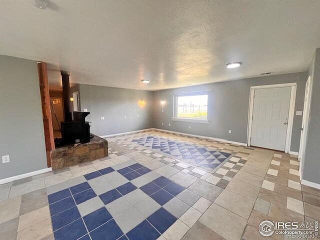 18542 County Road 8, Wiggins, CO 80654 - unfurnished living room featuring tile patterned floors, baseboards, and a wood stove