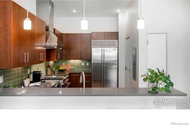 kitchen with sink, tasteful backsplash, wall chimney exhaust hood, hanging light fixtures, and high quality appliances