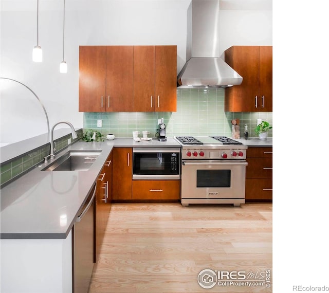 kitchen with stainless steel appliances, decorative backsplash, hanging light fixtures, sink, and wall chimney range hood