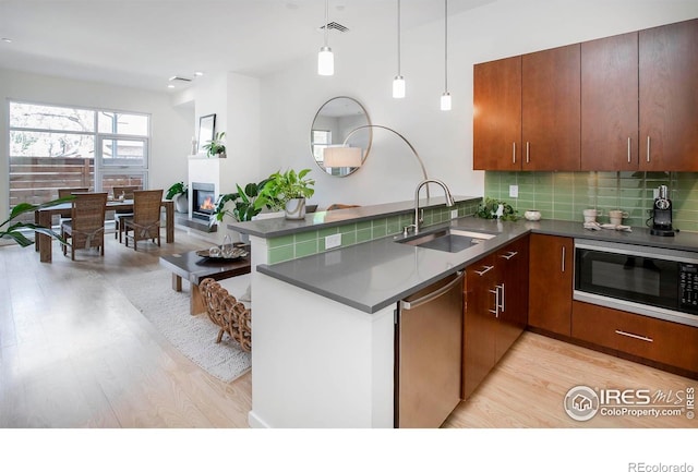 kitchen with appliances with stainless steel finishes, pendant lighting, sink, kitchen peninsula, and light hardwood / wood-style flooring