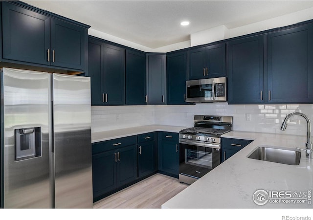 kitchen with light hardwood / wood-style floors, stainless steel appliances, light stone counters, sink, and tasteful backsplash