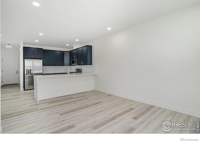 kitchen with stainless steel appliances, light wood-type flooring, backsplash, sink, and kitchen peninsula