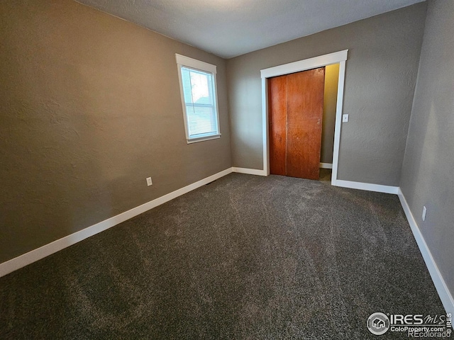 unfurnished bedroom featuring dark carpet, a textured ceiling, and a closet