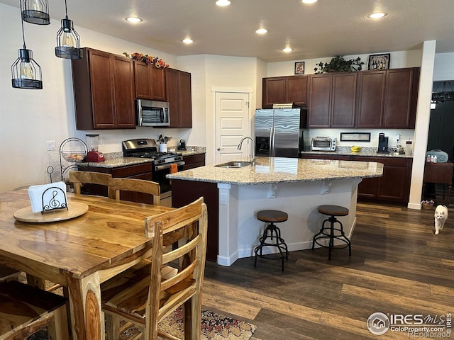 kitchen with sink, light stone counters, pendant lighting, stainless steel appliances, and a kitchen island with sink