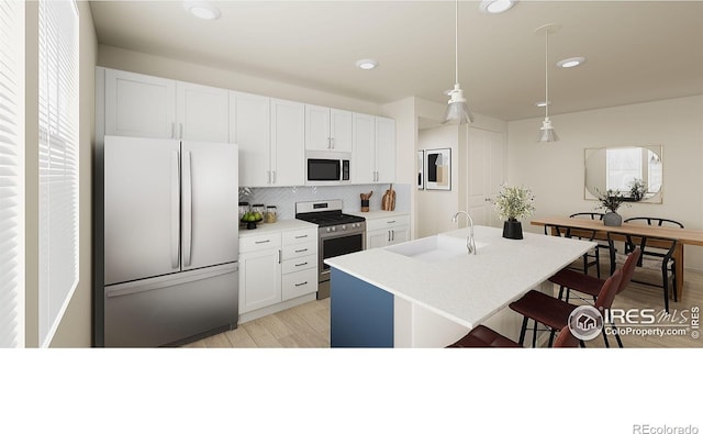 kitchen with stainless steel stove, sink, an island with sink, white cabinets, and refrigerator