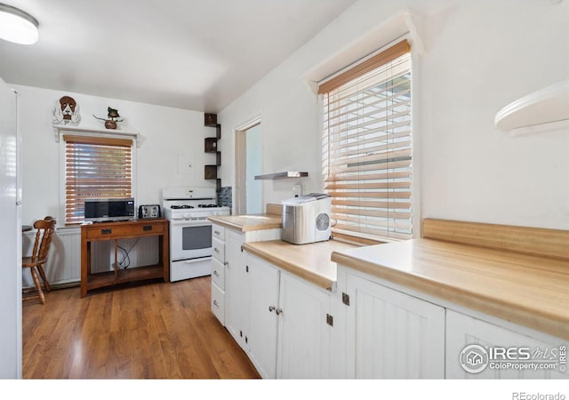 kitchen with wood-type flooring, white gas range, a healthy amount of sunlight, and white cabinets