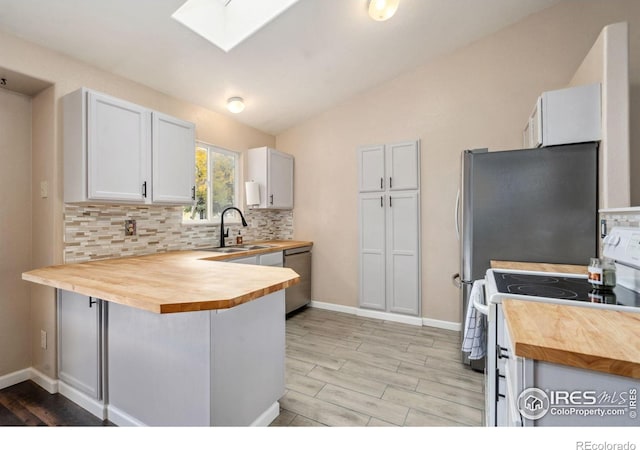 kitchen featuring stainless steel appliances, sink, butcher block countertops, lofted ceiling with skylight, and white cabinetry