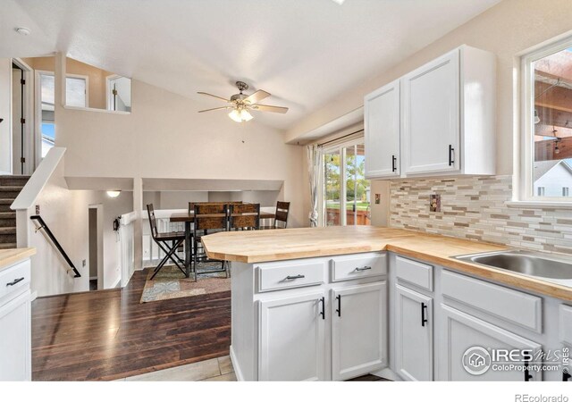 kitchen featuring wood-type flooring, white cabinetry, wood counters, decorative backsplash, and vaulted ceiling